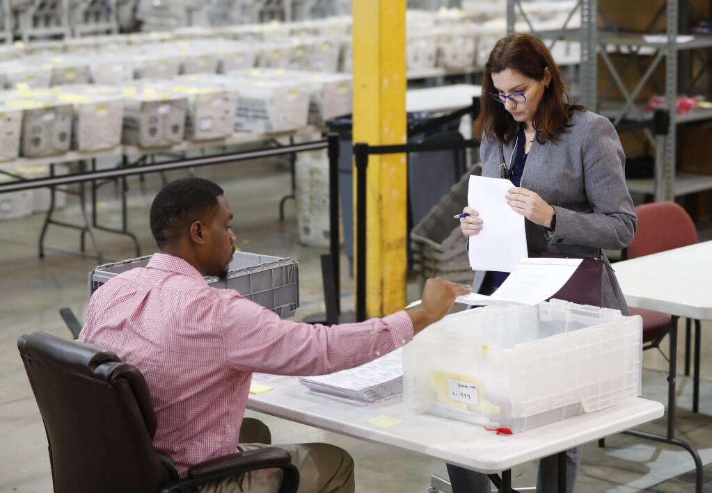 A Republican party observer, right, watches as an employee at the Palm Beach County Supervisor Of Elections office goes through a stack of damaged ballots, Thursday, Nov. 15, 2018, in West Palm Beach, Fla. A federal judge slammed Florida on Thursday for repeatedly failing to anticipate election problems, and said the state law on recounts appears to violate the U.S. Supreme Court ruling that decided the presidency in 2000. (AP Photo/Wilfredo Lee)