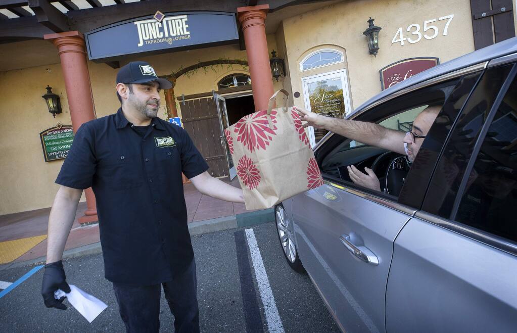 Peter Lopez Jr., owner of Juncture Taproom & Lounge, delivers a to-go food order and a growler of beer to David Magallon outside of his Santa Rosa restaurant on Wednesday, April 1, 2020. (John Burgess/The Press Democrat)