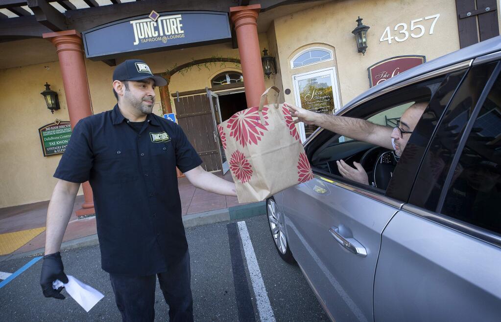 Peter Lopez Jr., owner of Juncture Taproom & Lounge, delivers a to-go food order and a growler of beer to David Magallon outside of his Santa Rosa restaurant on Wednesday, April 1, 2020. (John Burgess/The Press Democrat)