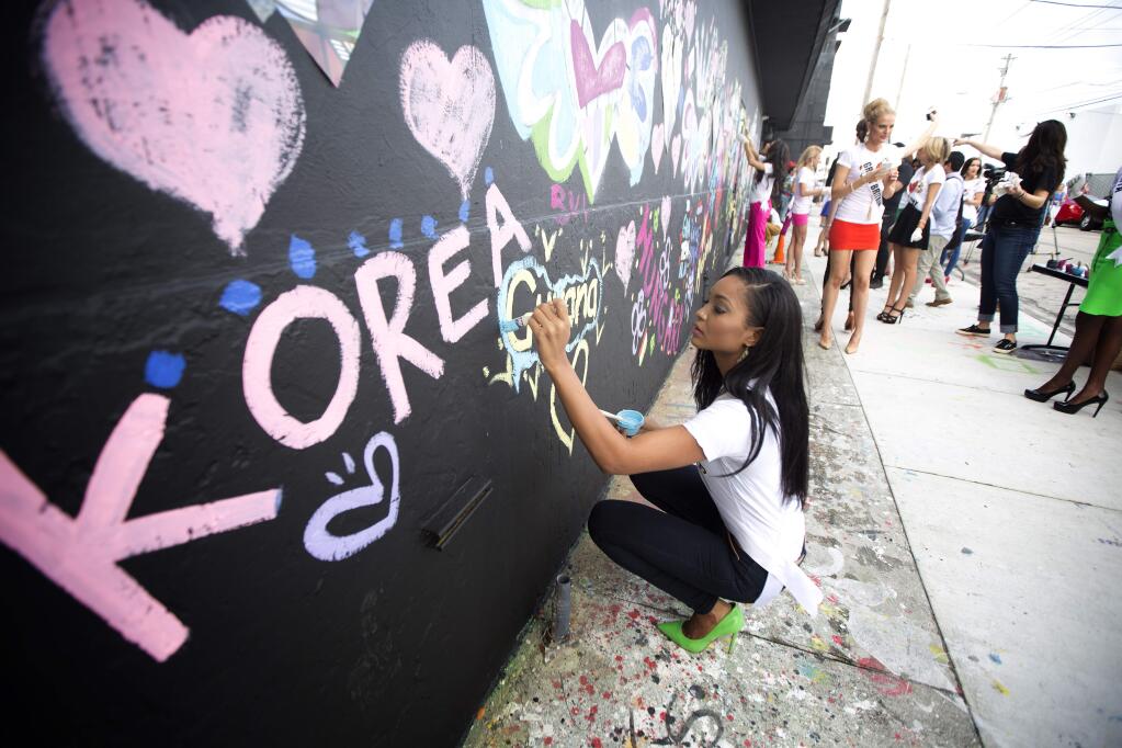Miss Guyana, Niketa Barker, paints on a wall in Miami's Wynwood area, Sunday, Jan. 11, 2015. Miss Universe contestants visited pop artist Romero Brittos studio for an interactive painting event. (AP Photo/J Pat Carter)