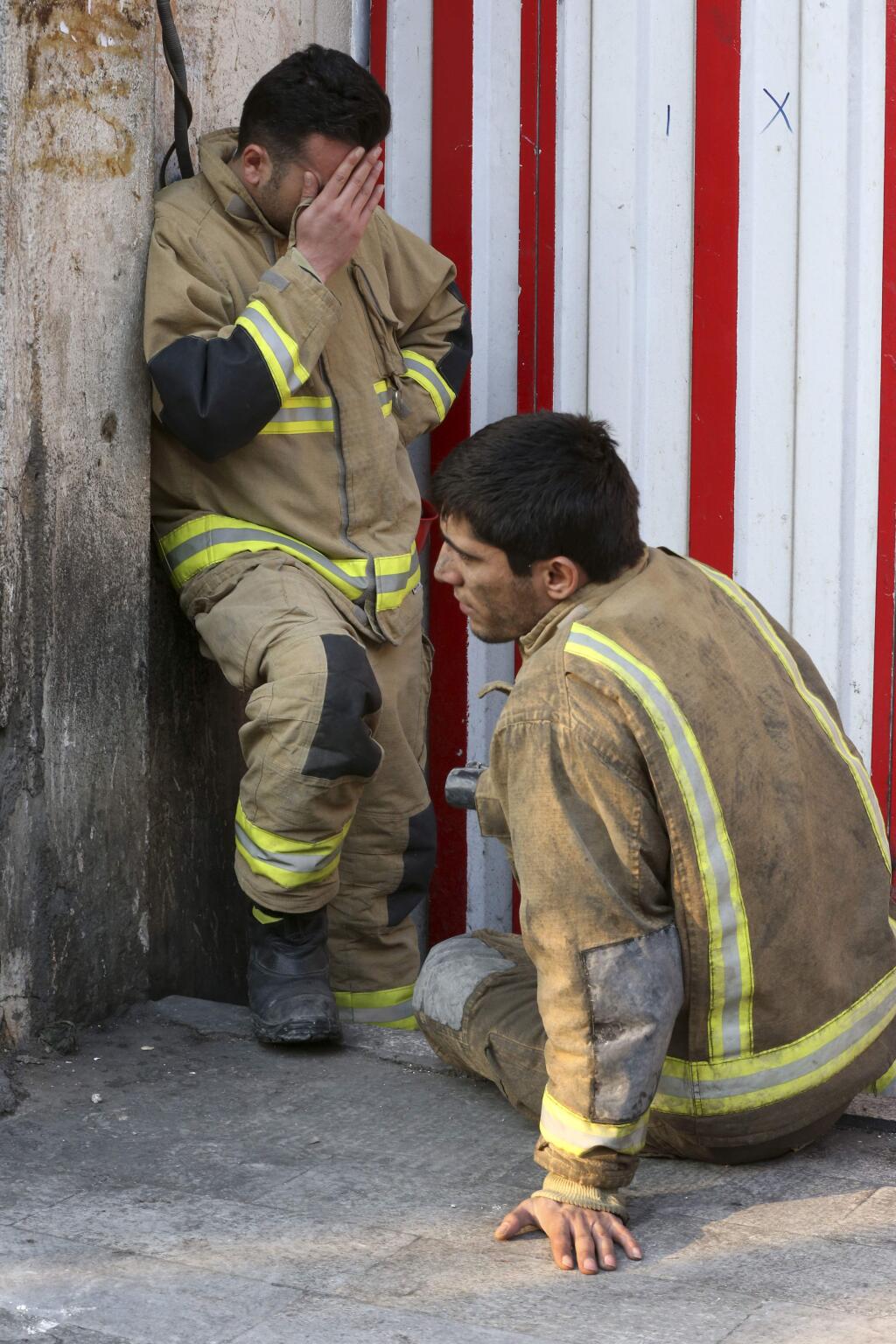An emotional firefighter stands next to his colleague outside to the Plasco building engulfed by a fire, in central Tehran, Iran, Thursday, Jan. 19, 2017. The disaster struck the iconic structure in central Tehran just north of the Iranian capital's sprawling bazaar. Firefighters, soldiers and other emergency responders dug through the rubble, looking for survivors. Dozens of firefighters were killed. (AP Photo/Vahid Salemi)