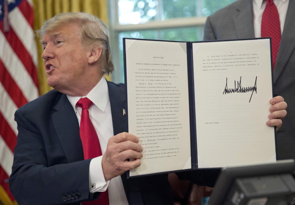 President Donald Trump holds up the executive order he signed Wednesday to end family separations at the border. (PABLO MARTINEZ MONSIVAIS / Associated Press)