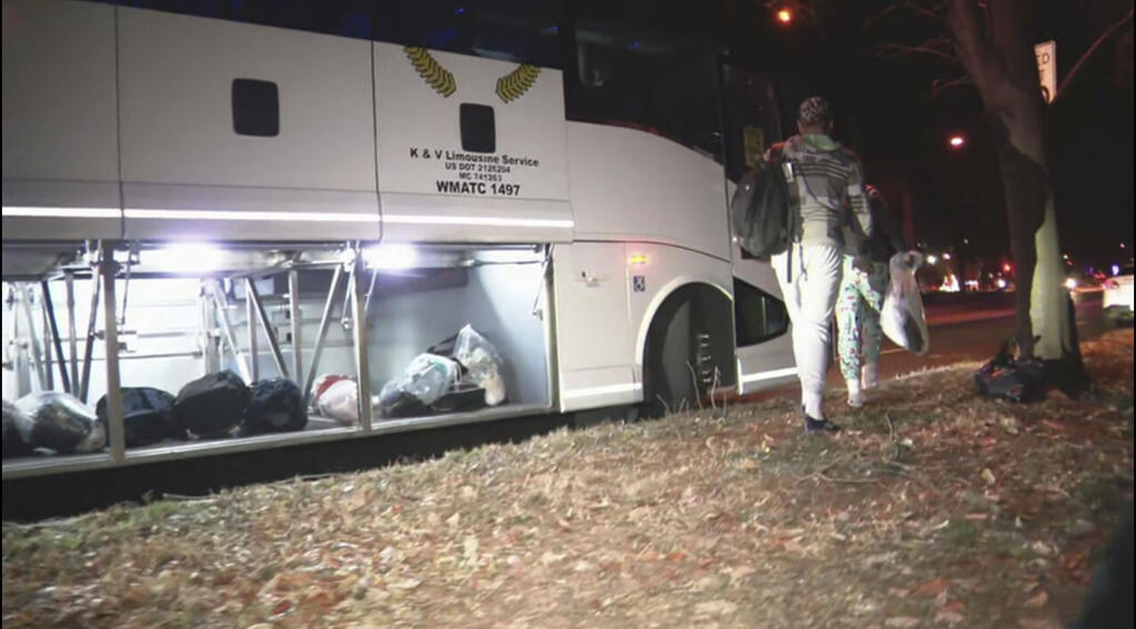 This image provided by WJLA shows migrant families as they get on a bus to transport them from near the Vice President's residence to an area church after they arrived in Washington, Saturday, Dec. 24, 2022. Local organizers in Washington say three buses of recent migrant families arrived from Texas near the home in record-setting cold on Christmas Eve. Texas authorities have not confirmed their involvement. (WJLA via AP)
