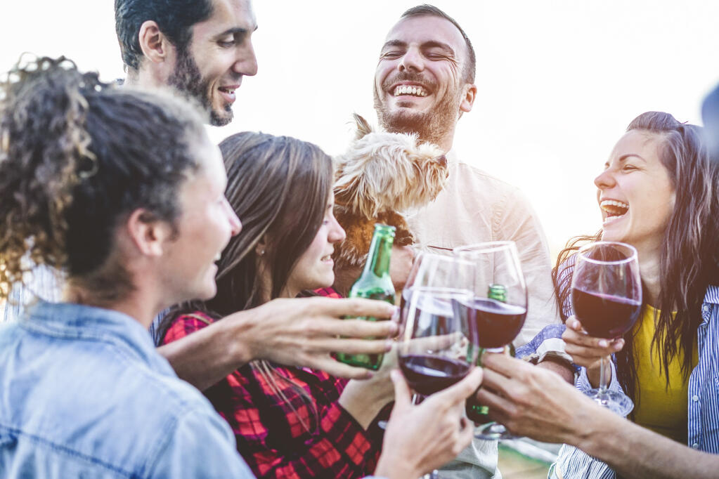 Group of young people laugh as they toast with wine glasses and beer bottles.