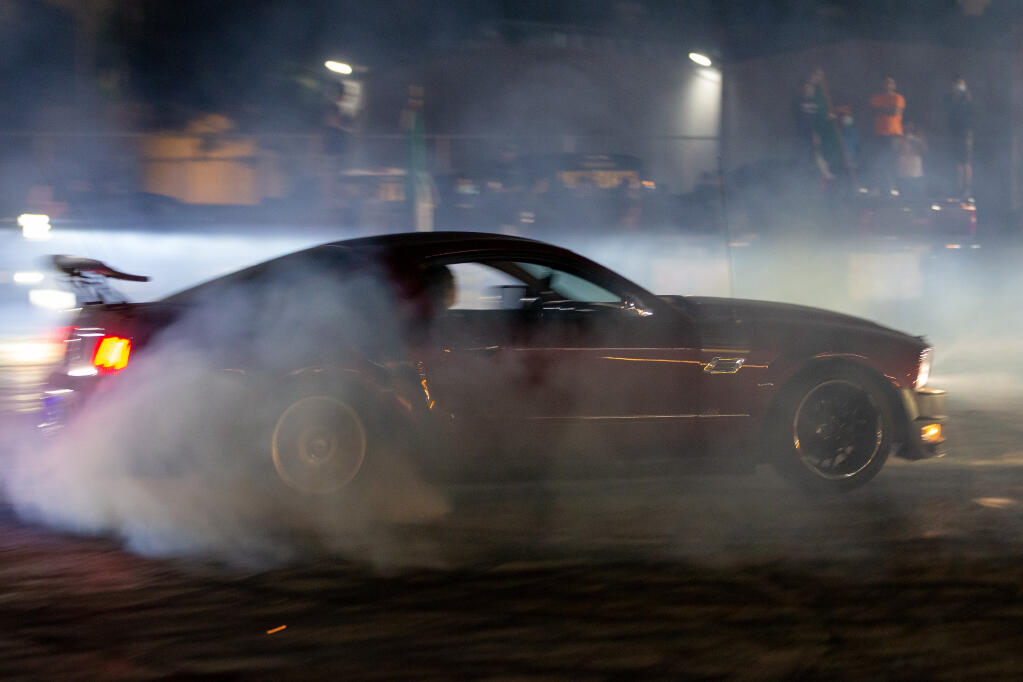 Smoke from a sports car's tires fill the air as its driver spins doughnuts during a sideshow at the Roseland Village Shopping Center in Santa Rosa, California, on Wednesday, Sep. 16, 2020. (Alvin A.H. Jornada / The Press Democrat)