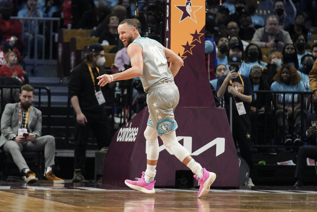 Golden State Warriors' Stephen Curry smiles as he points to the bench after hitting another three-point shot during the second half of the NBA All-Star basketball game, Sunday, Feb. 20, 2022, in Cleveland. (AP Photo/Charles Krupa)