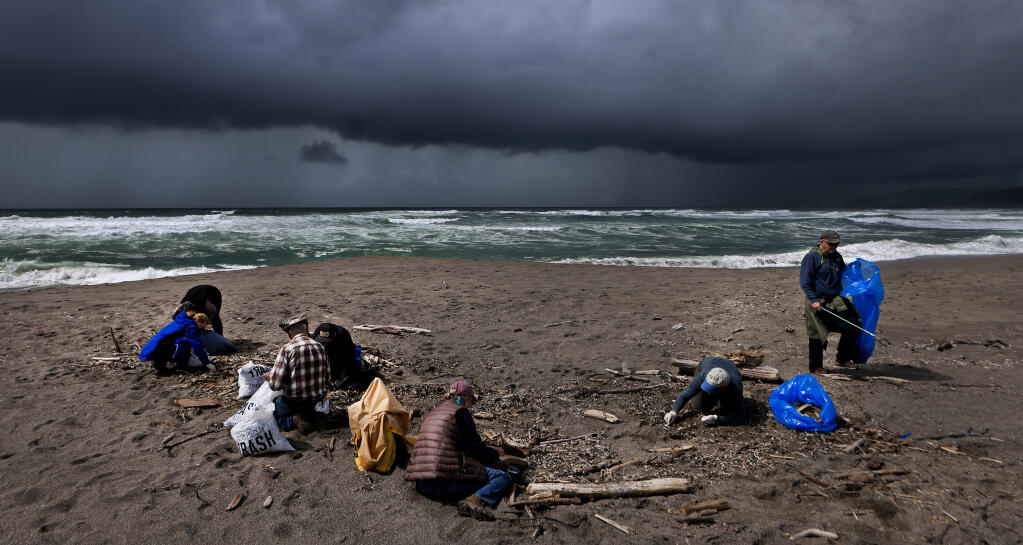 A thunderstorm bears down on volunteers with Coastwalk California as they resort to ground level work picking up bits of styrofoam from the Aleutian Storm fishing vessel. Saturday, March 23, 2024, that was beached in February at Salmon Creek Beach south, at Bodega Dunes State Park. (Kent Porter / The Press Democrat)