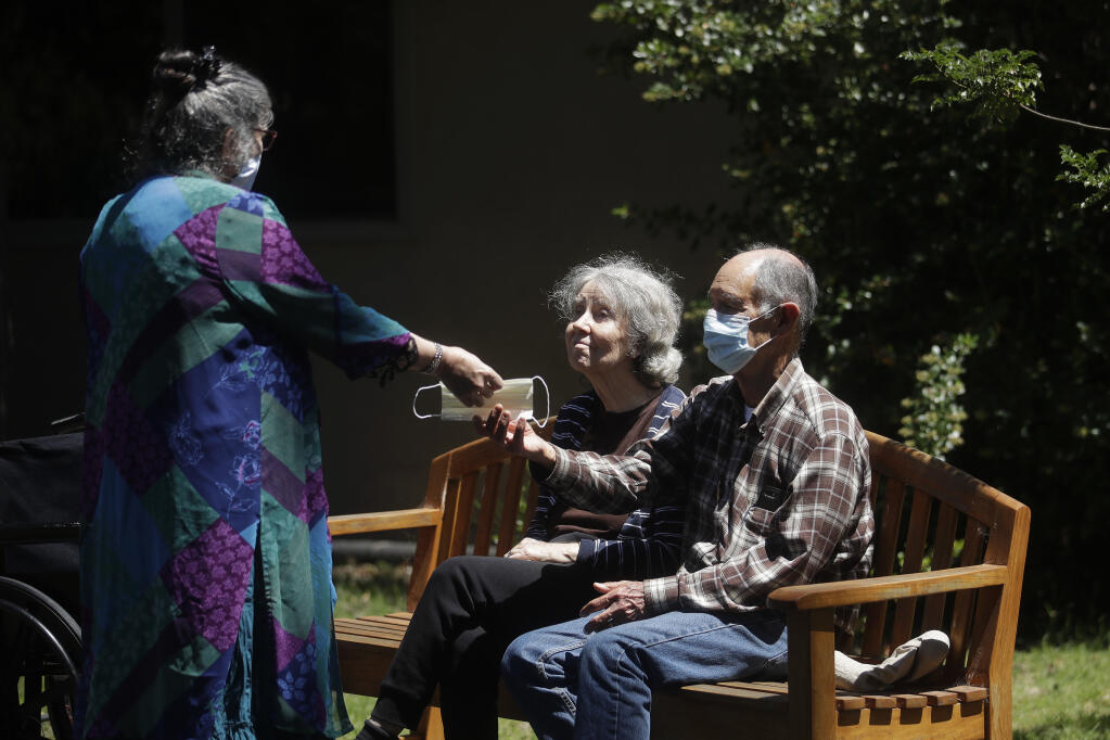 Chaparral House executive director KJ Page, left, hands a mask to Larry Yarbroff, right, as he sits with his wife, Mary, while visiting her at Chaparral House in Berkeley, Calif., Friday, July 10, 2020. (AP Photo/Jeff Chiu)