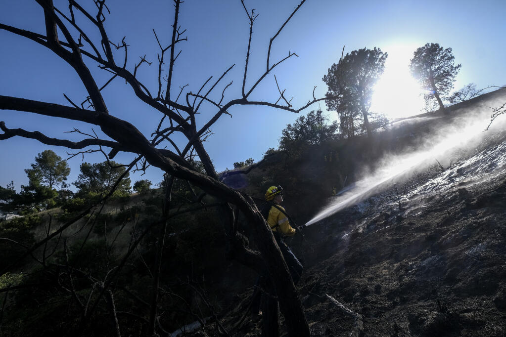 A firefighter sprays water on hot spots during a brushfire near the Griffith Observatory in the hills of Los Feliz in Los Angeles on Tuesday, May 17, 2022. (AP Photo/Ringo H.W. Chiu)