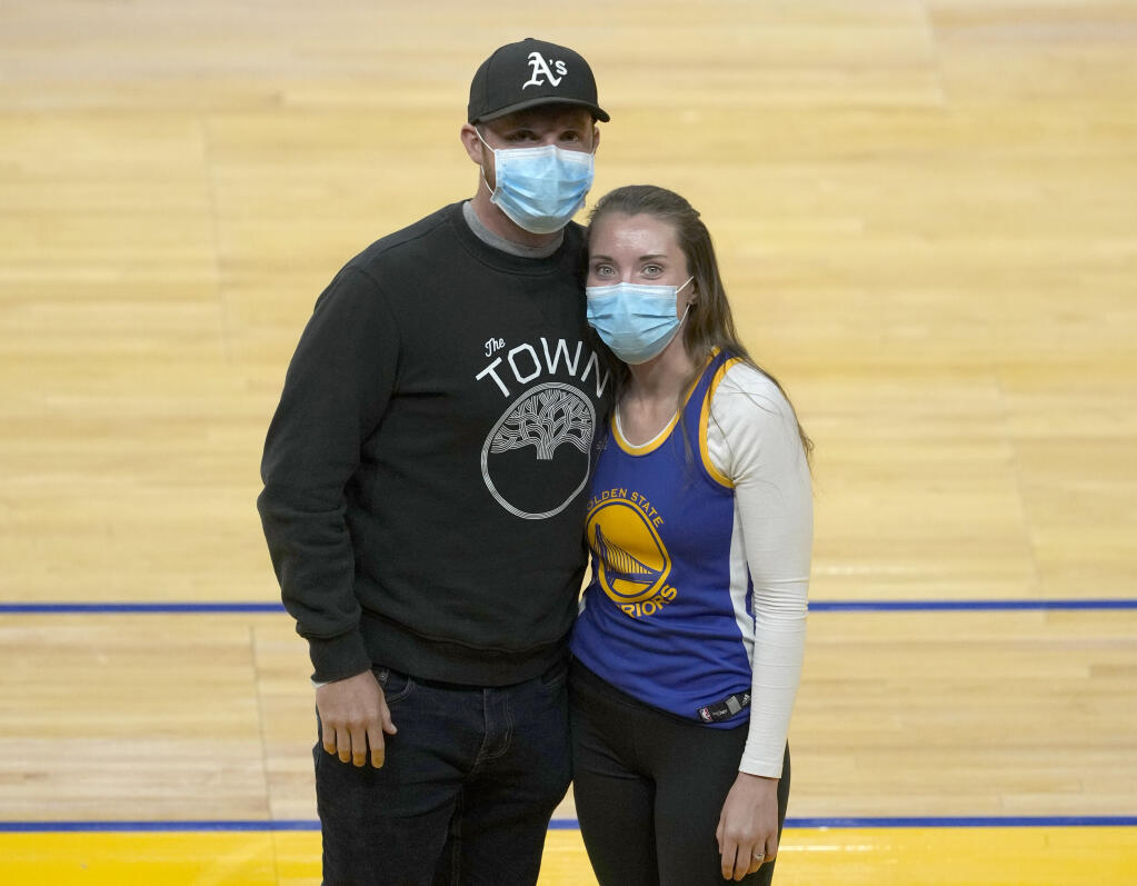 Shelby Delaney, right, an intensive care unit nurse at Oakland's Alta Bates Summit Medical Center, and her husband, Robert Crowley, pose for a photo before the Golden State Warriors and Sacramento Kings NBA basketball game on Sunday, April 25, 2021, in San Francisco. Last spring, Stephen Curry placed a FaceTime call to Delaney and her colleagues at Oakland's Alta Bates Summit Medical Center after learning she was wearing his No. 30 jersey under her scrubs as inspiration to get through each trying day of the pandemic. Delaney wore the uniform again as she and Crowley sat on the floor for Sunday's game after a season ticket holder who couldn't attend gifted her the seats. Inside the jersey reads, "I Can Do All Things." (AP Photo/Tony Avelar)