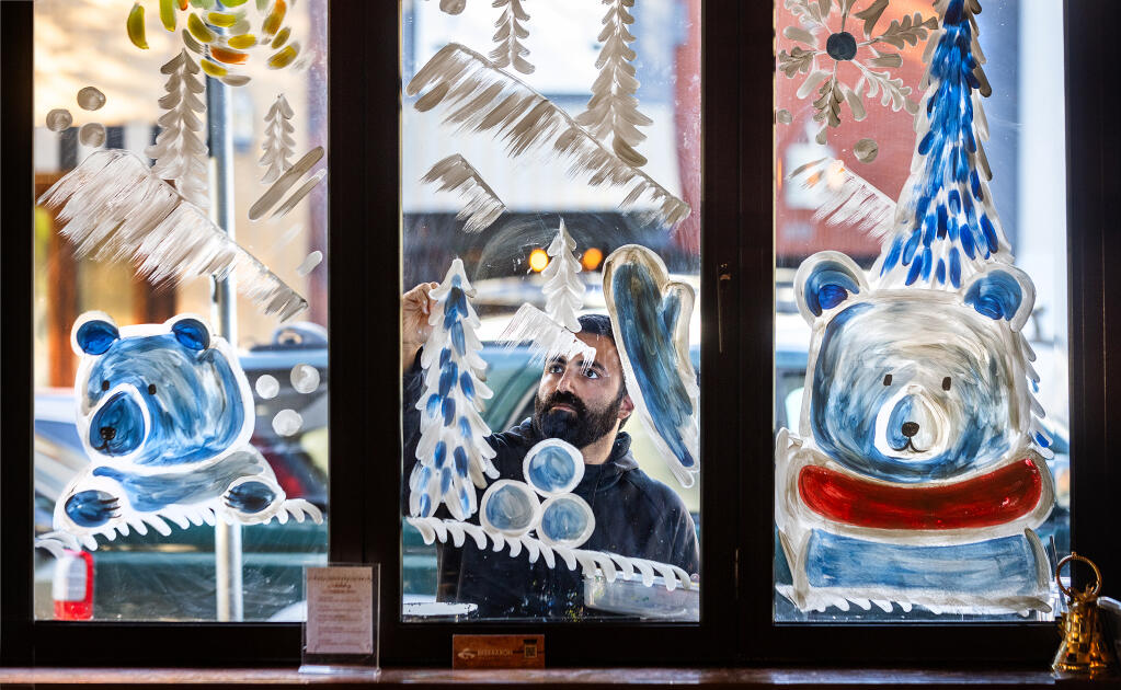 Clifton Gold paints a holiday scene with polar bears on the windows of Beer Baron Whiskey Bar & Kitchen, Monday, Dec. 4, 2023, on Old Courthouse Square in Santa Rosa. Gold makes extra money during the holidays on his “side hustle,” while bringing some cute Christmas spirit to downtown Santa Rosa. (John Burgess / The Press Democrat)