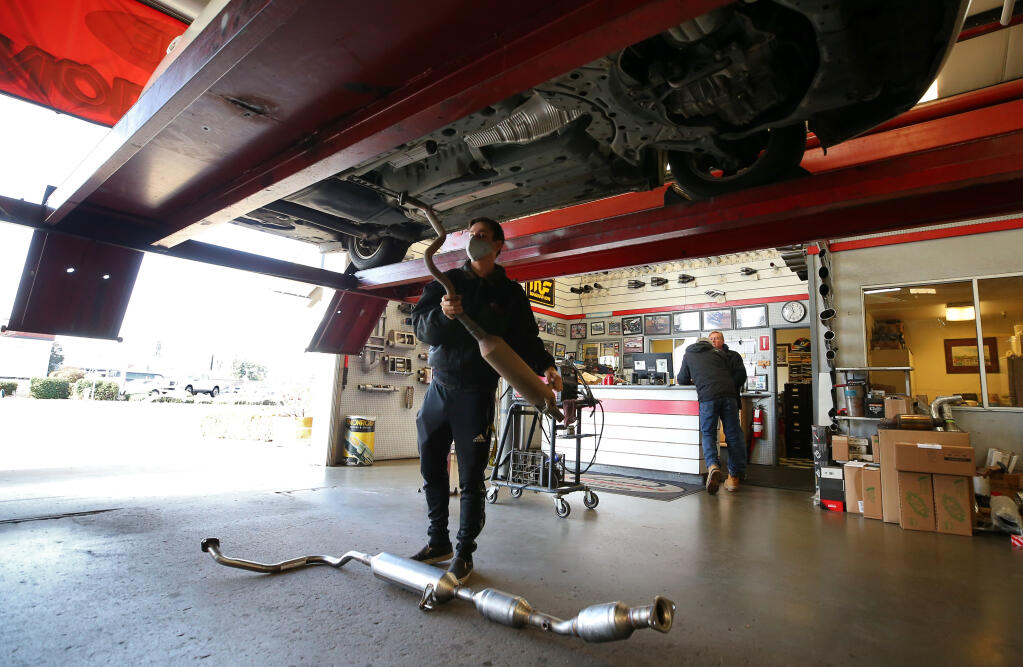 Jesse Martin removes the exhaust resonator, which thieves cut off and stole the catalytic converters, before a new unit, seen on the floor, is installed Monday, Jan. 12, 2021, on a Toyota Prius at Johnny Franklin’s Muffler in Santa Rosa. The converters contain platinum and rhodium in liquid form that when extracted can fetch high prices. (Christopher Chung / The Press Democrat)