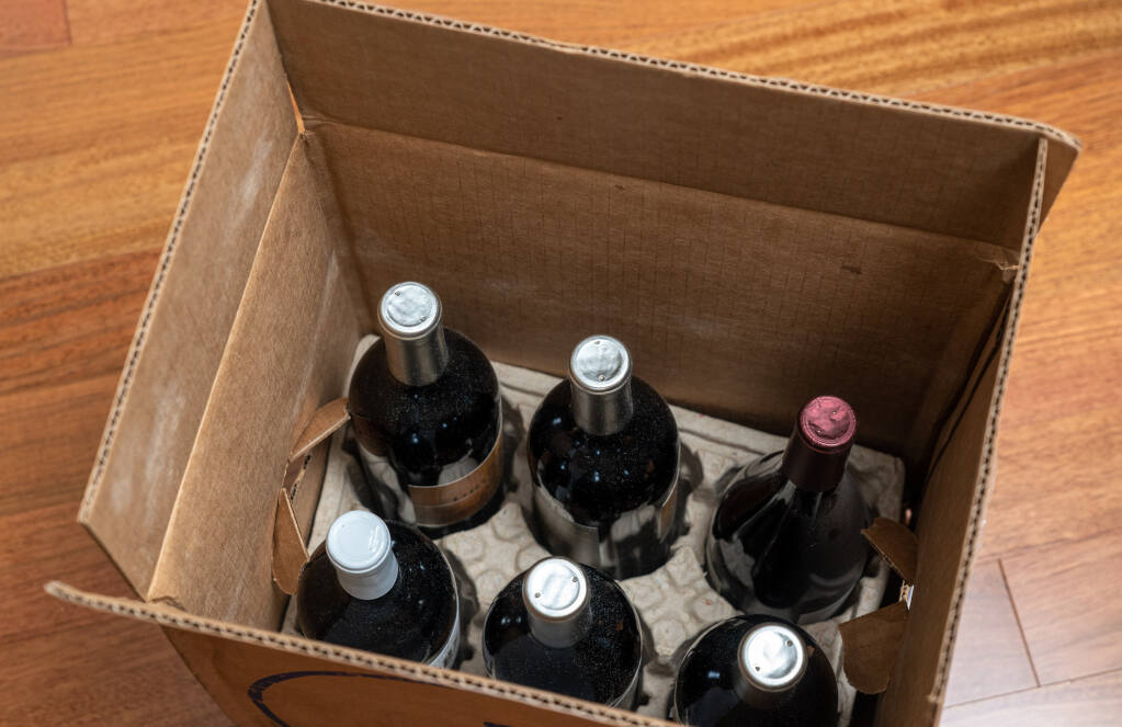 Open box of a half-dozen bottles (half-case) of wine sits on wooden floor, illustrating direct-to-consumer home delivery.