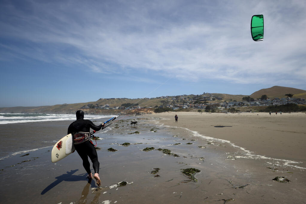 Steve Dunlop of Santa Rosa walks his kite and surfboard down the beach after uncooperative winds at Dillon Beach near Tomales, Calif. on Thursday, May 19, 2022. (Beth Schlanker/The Press Democrat)