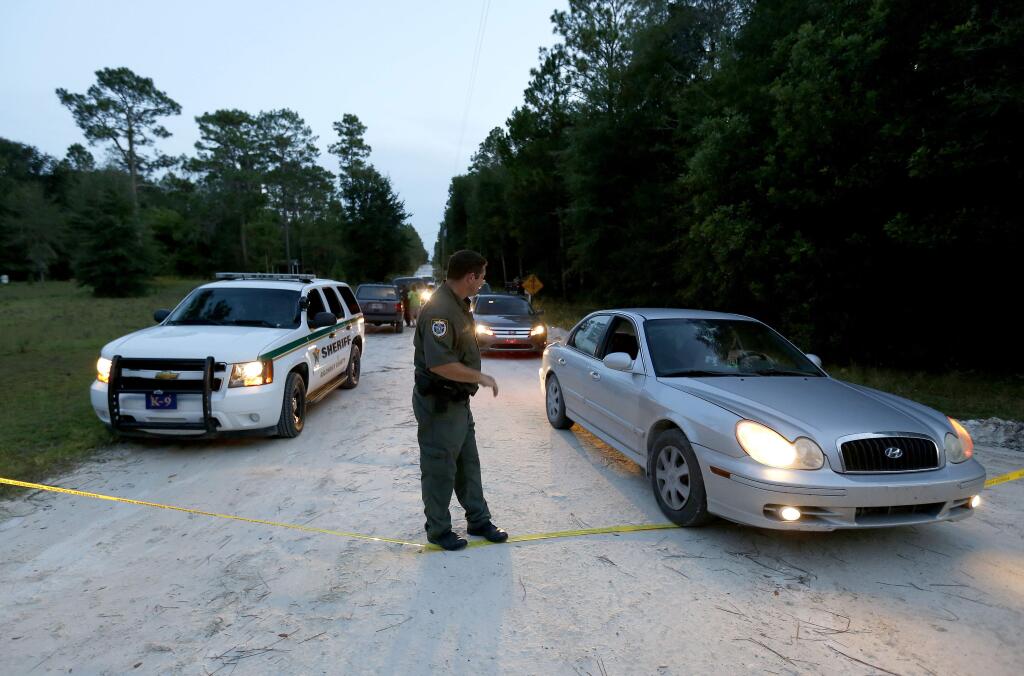 A Gilchrist County sheriff's deputy lowers the yellow tape to let vehicles through at the scene of a shooting on Thursday, Sept. 18, 2014 in Bell, Fla. (AP Photo/The Gainesville Sun, Matt Stamey)