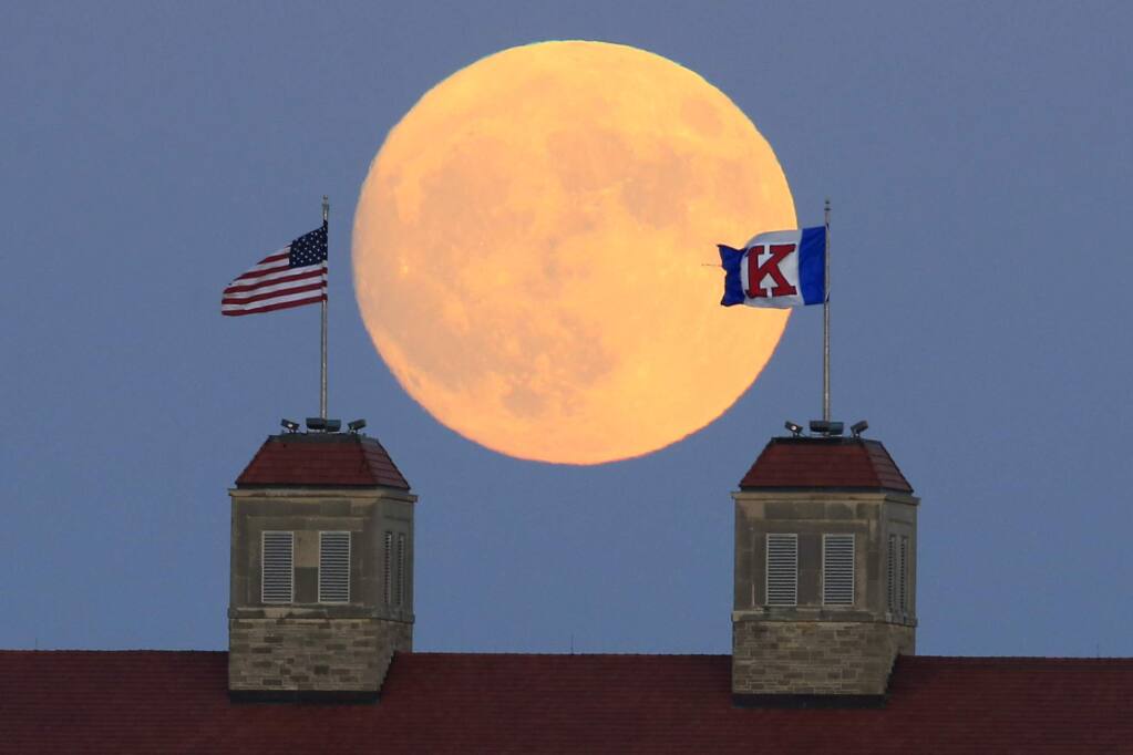 The moon rises beyond flags atop Fraser Hall on the University of Kansas campus in Lawrence, Kan., Sunday, Nov. 13, 2016. Monday morning's supermoon was to be the closest a full moon has been to Earth since Jan. 26, 1948. (AP Photo/Orlin Wagner)