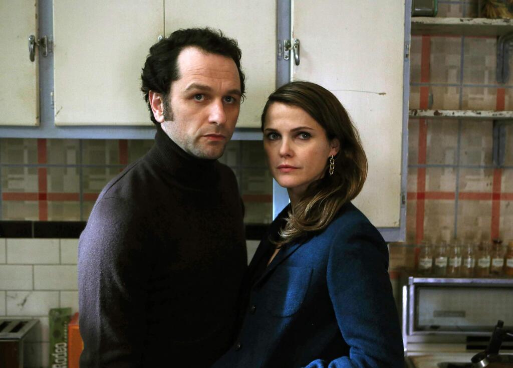 In this image released by FX, Matthew Rhys, left, and Keri Russell appear in a scene from 'The Americans.' The show will conclude its series run on FX with two more seasons, the network announced Wednesday, May 25, 2016. A 13-episode fifth season will air in 2017, followed by a 10-episode sixth and final season in 2018, FX said. (Craig Blankenhorn/FX via AP)
