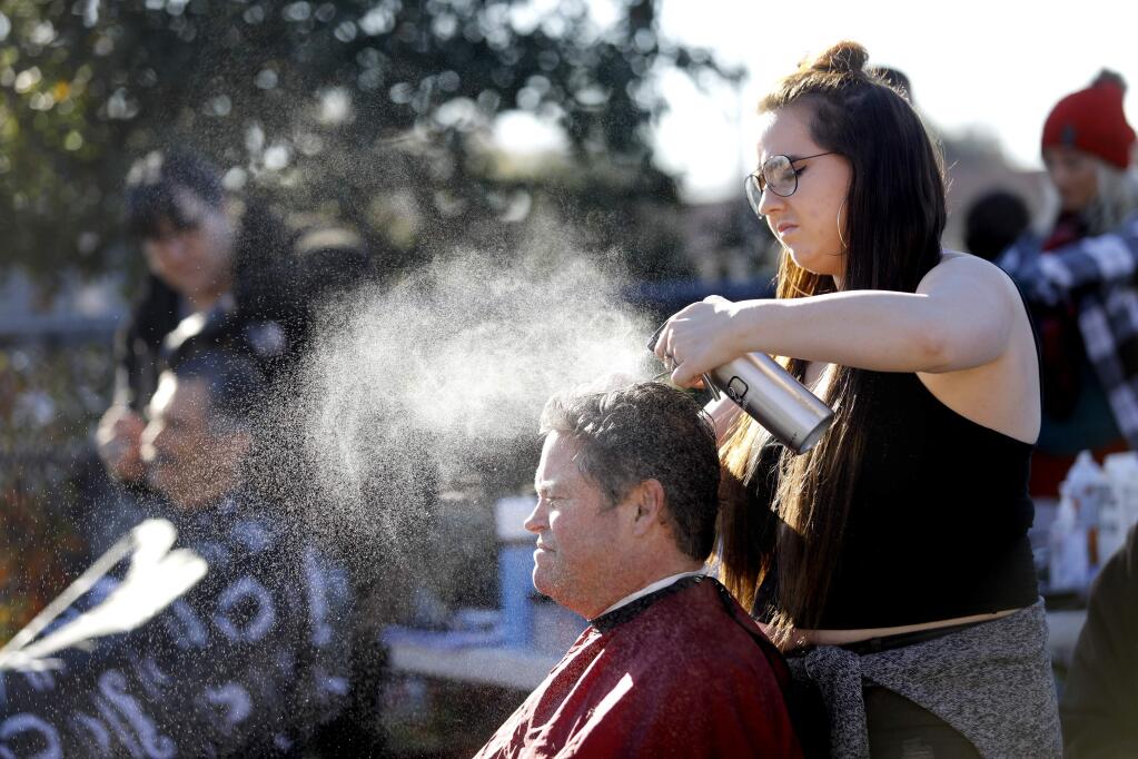 Kayla Tracy, a barbering student, spritzes water on Jess Quarles hair during a Haircuts for the Homeless event at the Arlene Francis Center in Santa Rosa on Sunday, Dec. 17, 2017. (PD STAFF)