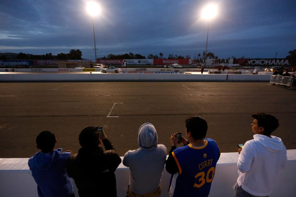 A group of spectators watches the races from behind the safety of a distant wall during Wednesday Night Drags at Sonoma Raceway on Wednesday, April 13, 2016. (Alvin Jornada / The Press Democrat)