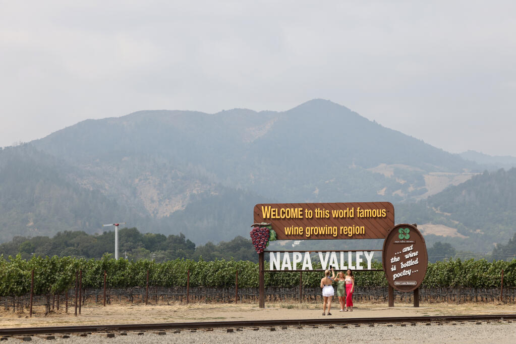 Women pose for a photo near the Welcome to Napa Valley sign as drifting wildfire smoke creates a hazy sky in Oakville, Monday, Aug. 21, 2023. (Beth Schlanker / The Press Democrat file)