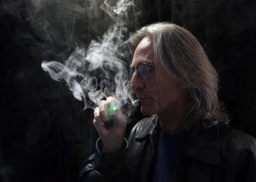 FILE - In this Dec. 4, 2013, file photo, John Hartigan, proprietor of Vapeology LA, a store selling electronic cigarettes and related items, takes a puff of an electronic cigarette at his store in Los Angeles. (AP Photo/Reed Saxon, File)
