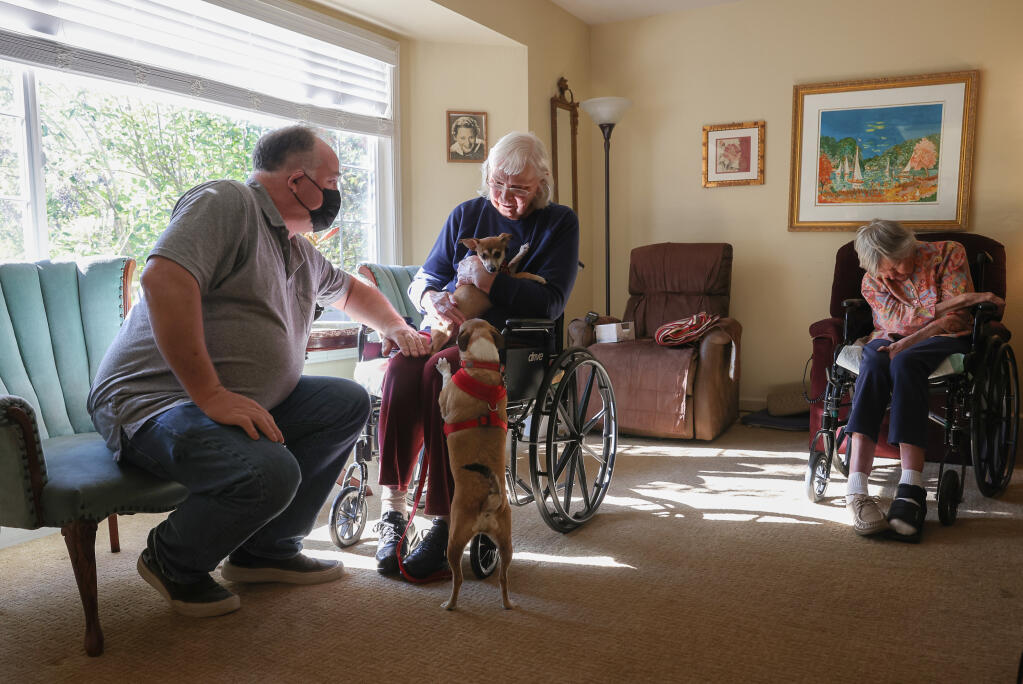 John Schoonover, left, talks with Dorothy Guenter as she pets his dogs Frida Maria and Bandita Dora at his Windsor House care home in Windsor on Tuesday, Nov. 15, 2022. (Christopher Chung/The Press Democrat)