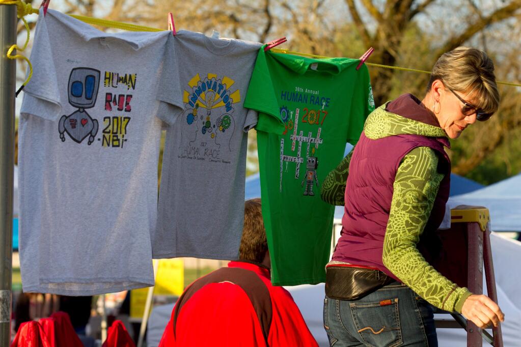 Volunteer Julie Owens hangs up several Human Race T-shirts for judging in a T-shirt contest before the race, during early morning preparations for The Human Race, in Santa Rosa, Calif., on Saturday, May 6, 2017. (Photo by Darryl Bush / For The Press Democrat)