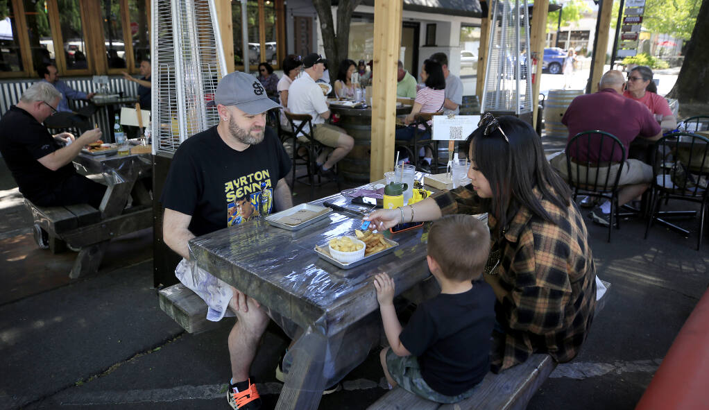 The Yates family of Todd, left, Takota, 3, and Sam, eat at the outdoor venue of KINSmoke in Healdsburg, Tuesday, May 4, 2021.  This is the first vacation the family from San Jose has taken since the pandemic began in 2020. They are both fully vaccinated.   (Kent Porter / The Press Democrat) 2021