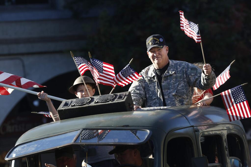 Retired National Guard Major Bill Simmons and Peter Lind, 10, wave flags atop a vintage military vehicle during the Veterans Day parade on Wednesday, November 11, 2015 in Petaluma, California . (BETH SCHLANKER/ The Press Democrat)