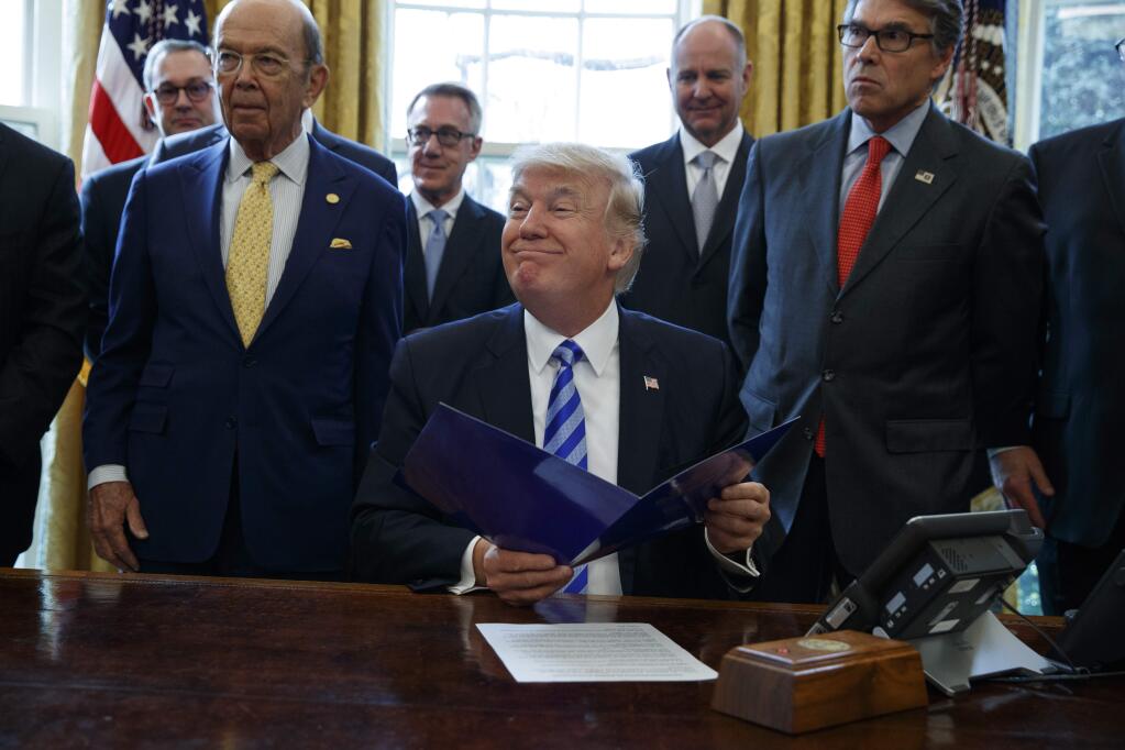FILE - In this March 24, 2017 file photo, President Donald Trump, flanked by Commerce Secretary Wilbur Ross, left, and Energy Secretary Rick Perry, is seen in the Oval Office of the White House in Washington, during the announcing of the approval of a permit to build the Keystone XL pipeline, clearing the way for the $8 billion project.A federal judge in Montana has blocked construction of the $8 billion Keystone XL Pipeline to allow more time to study the project's potential environmental impact. U.S. District Judge Brian Morris' order on Thursday, Nov. 8, 2018, came as Calgary-based TransCanada was preparing to build the first stages of the oil pipeline in northern Montana. Environmental groups had sued TransCanada and The U.S. Department of State in federal court in Great Falls. (AP Photo/Evan Vucci, File)