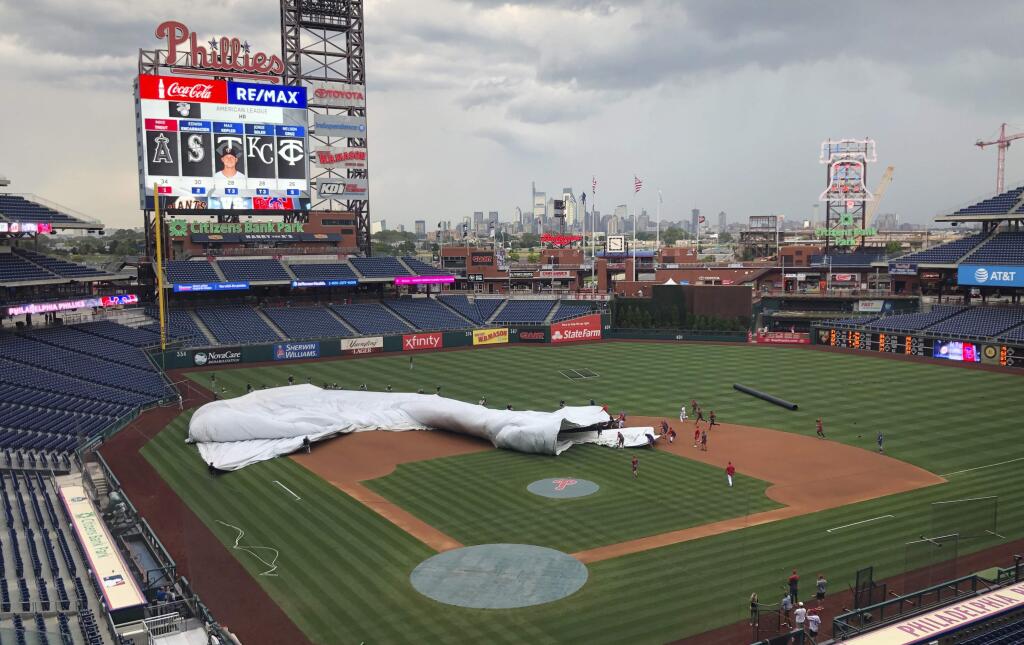 Members of the San Francisco Giants and Philadelphia Phillies join the grounds crew at Citizens Bank Park to help put the tarp on the field several hours before a scheduled baseball game in Philadelphia on Wednesday, July 31, 2019. A sudden burst of wind sent the tarp flapping, and players rushed in to help weigh it down. (AP Photo/Rob Maaddi)