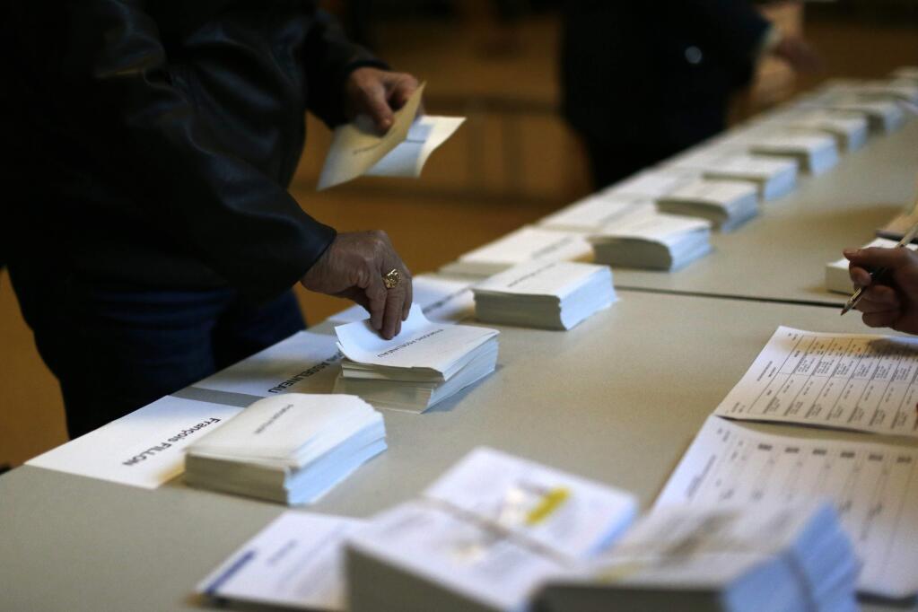 A man picks a ballot paper before voting for the first-round presidential election at a polling station in Paris, Sunday, April 23, 2017. French voters are casting ballots for their next president in an unusually close first-round election Sunday, after a campaign dominated by concerns about jobs and immigration and clouded by security fears following a recent attack on police guarding the Champs-Elysees in Paris. (AP Photo/Emilio Morenatti)