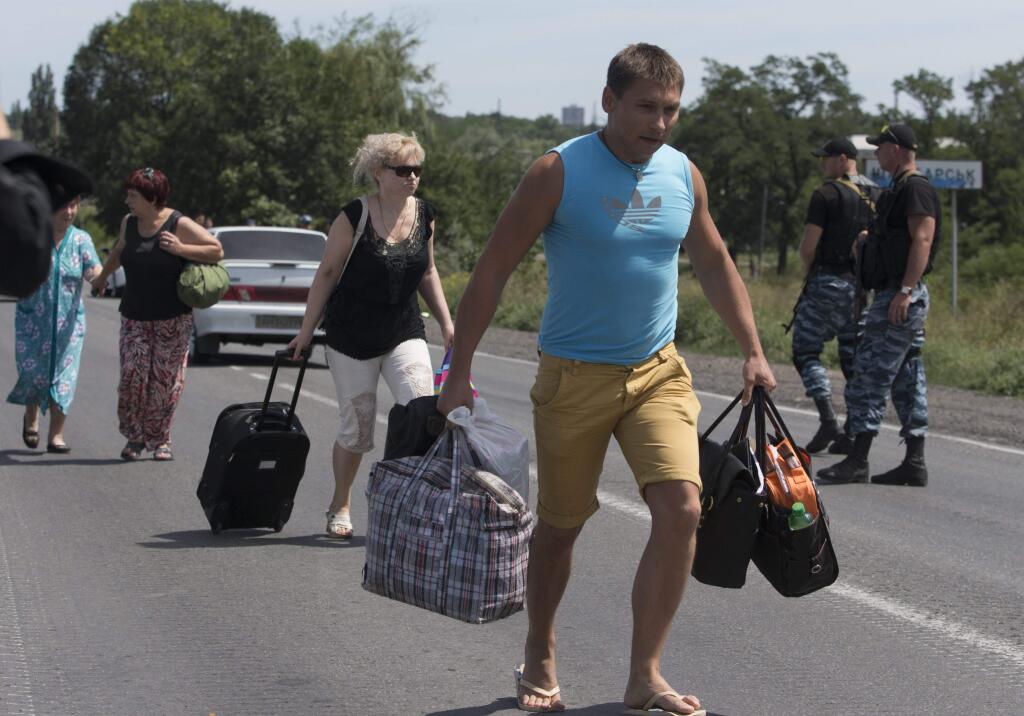 Self-proclamed Donetsk People's Republic policemen watch refugees fleeing Shakhtarsk, Donetsk region, eastern Ukraine on Monday, July 28, 2014. An international police team abandoned its attempt to reach the crash site of a Malaysia Airlines plane for a second day running Monday as clashes raged in a town on the road to the area.(AP Photo/Dmitry Lovetsky)