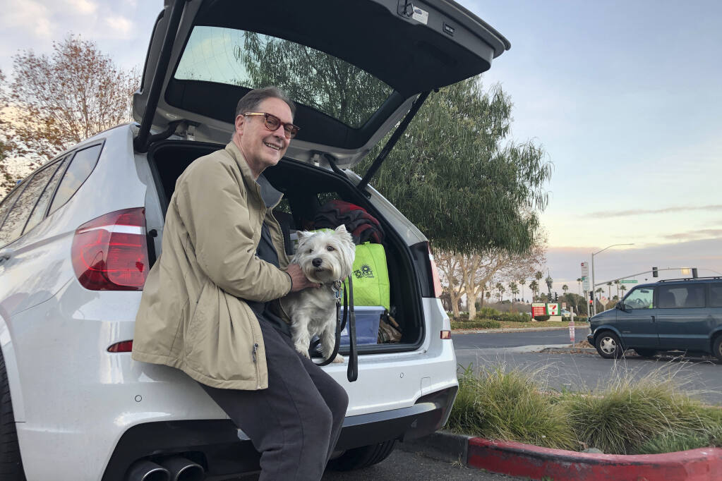 Matt Frinzi, 68, poses with his dog, Whitey, and his car filled with his belongings, in West Sacramento, California, on Tuesday, Dec. 15, 2020. Prinzi has lived in California for 25 years. But Tuesday he officially moved to Reno, Nevada. He said his quality of life has deteriorated so much in California that he wanted to leave. California saw its slowest growth rate on record for the nation's most populous state, adding just 21,200 people during the year that ended in July, state officials said Wednesday, Dec. 16, 2020. (AP Photo/Adam Beam)