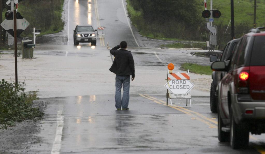 A man checks out the water running over Ely Road North just south of Old Redwood Highway during heavy rains on Thursday, December 11, 2014. (SCOTT MANCHESTER/ARGUS-COURIER STAFF)