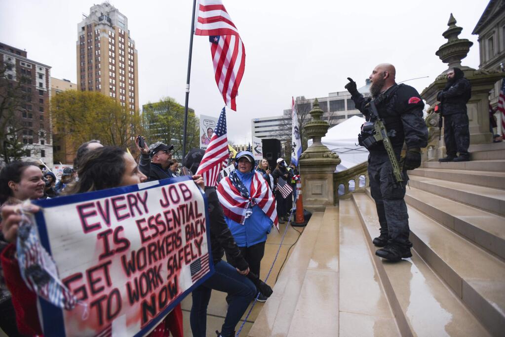 Members of the Michigan Liberty Militia, including Phil Robinson, right, join protesters at a rally at the state Capitol in Lansing, Mich., Thursday, April 30, 2020. Hoisting American flags and handmade signs, protesters returned to the state Capitol to denounce Gov. Gretchen Whitmer's stay-home order and business restrictions due to COVID-19, while lawmakers met to consider extending her emergency declaration hours before it expires. (Matthew Dae Smith/Lansing State Journal via AP)