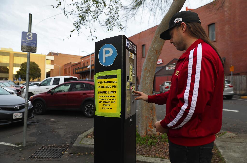 Taylor Frey pays for parking in a lot on 5th Street, where a sign informs the public of the new paid parking enforcement times, in Santa Rosa on Friday, January 26, 2018. (Christopher Chung/ The Press Democrat)