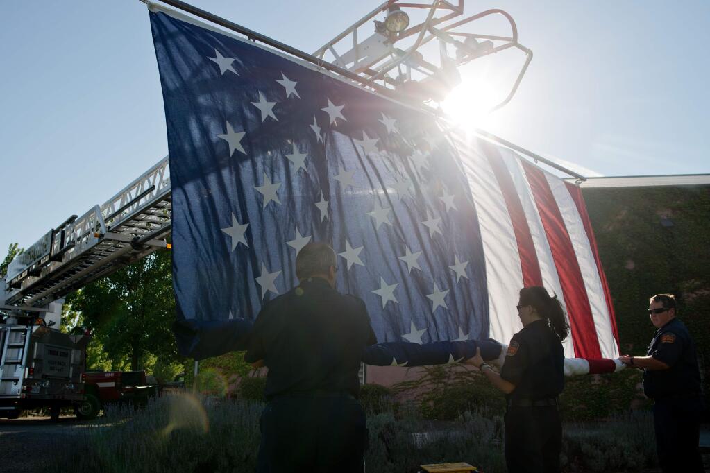 Healdsburg Firefighters Mike Dale, left, Amanda Newhall and Robert Salisbury unfurl a 25-foot flag suspended from the Healdsburg Fire Department ladder truck as the National Anthem is sung, during Wine Country to the Rescue, a fundraiser to benefit the fire departments of Geyserville, Cloverdale, and Healdsburg, and the communities they serve, held at Clos du Bois Winery in Geyserville, California, on July 19, 2014. (Alvin Jornada / For The Press Democrat)