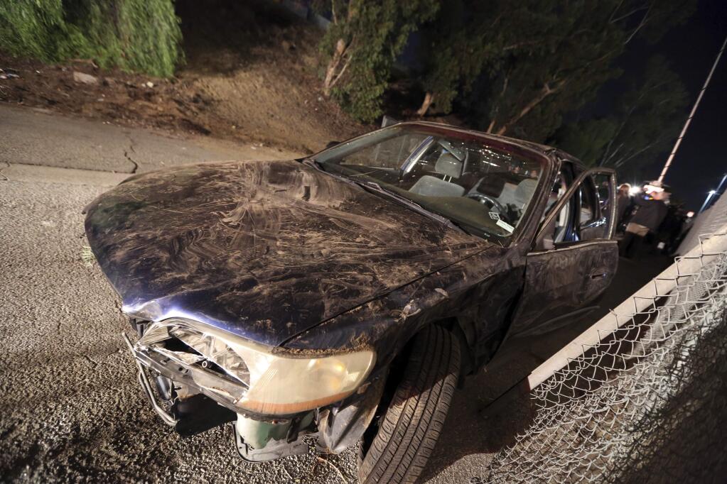A car that went off the side of the southbound lanes of Interstate 405 and landed on a homeless encampment is seen after it was pulled from the scene, left rear, near Sherman Way in the Van Nuys area of Los Angeles, Tuesday, Nov. 29, 2016. A woman who may have been homeless was killed and three people in the car were injured. (AP Photo/Reed Saxon)