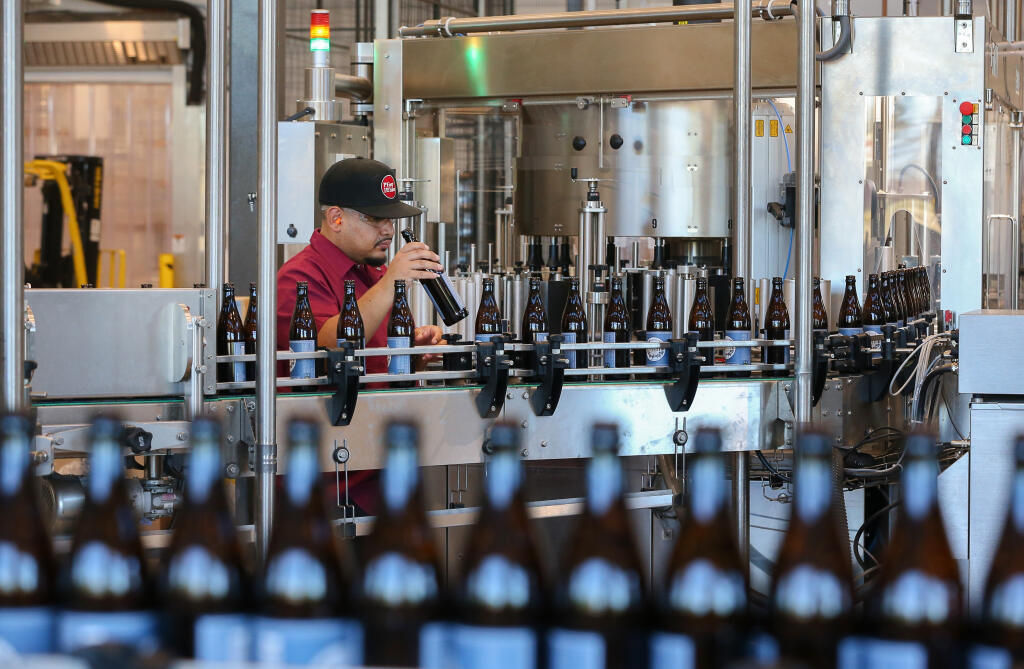 Juan Perez checks bottles before they are filled with Pliny the Younger at the Russian River Brewing Company facility in Windsor on Tuesday, March 22, 2022. (Christopher Chung/ The Press Democrat)