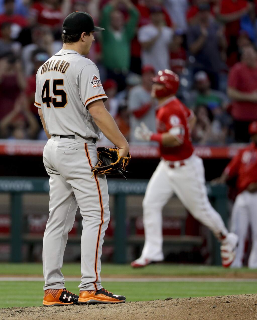 San Francisco Giants starting pitcher Derek Holland, left, watches as Los Angeles Angels' Mike Trout rounds the bases after a home run during the third inning in Anaheim, Saturday, April 21, 2018. (AP Photo/Chris Carlson)
