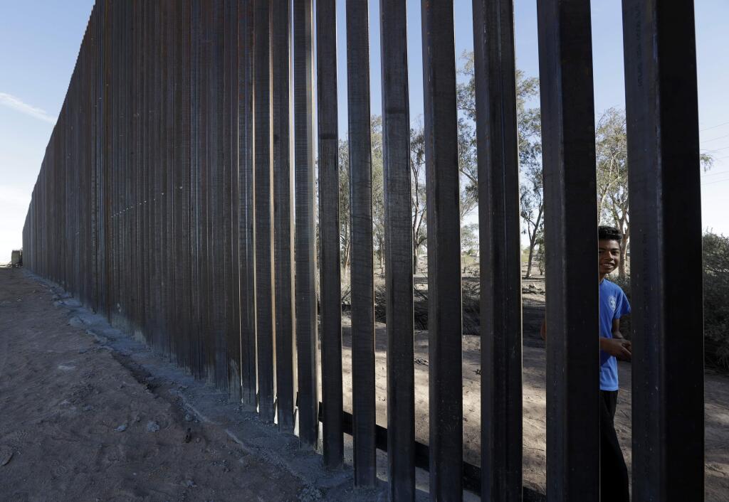 In this March 5, 2018, photo, a boy looks through the first section of a newly-constructed structure along the border separating Mexicali, Mexico, right, and Calexico, Calif. (AP Photo/Gregory Bull)