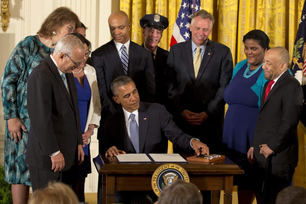 Surrounded by LGBT supporters, including Virginia Governor Terry McAuliffe, third from right, President Barack Obama signs executive orders to protect LGBT employees from federal workplace discrimination in the East Room of the White House Monday, July 21, 2014, in Washington. (AP Photo/Jacquelyn Martin)