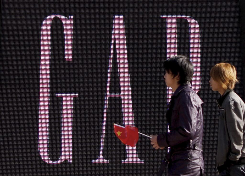 FILE - In this Nov. 16, 2010 file photo, a man carries a Chinese flag as he walks past U.S. retailer GAP's newly-opened flagship store in Beijing. U.S. clothing retailer Gap has apologized Monday, May 14, 2018, for selling T-shirts with what it says was an 'erroneous' map of China. (AP Photo/Andy Wong, File)
