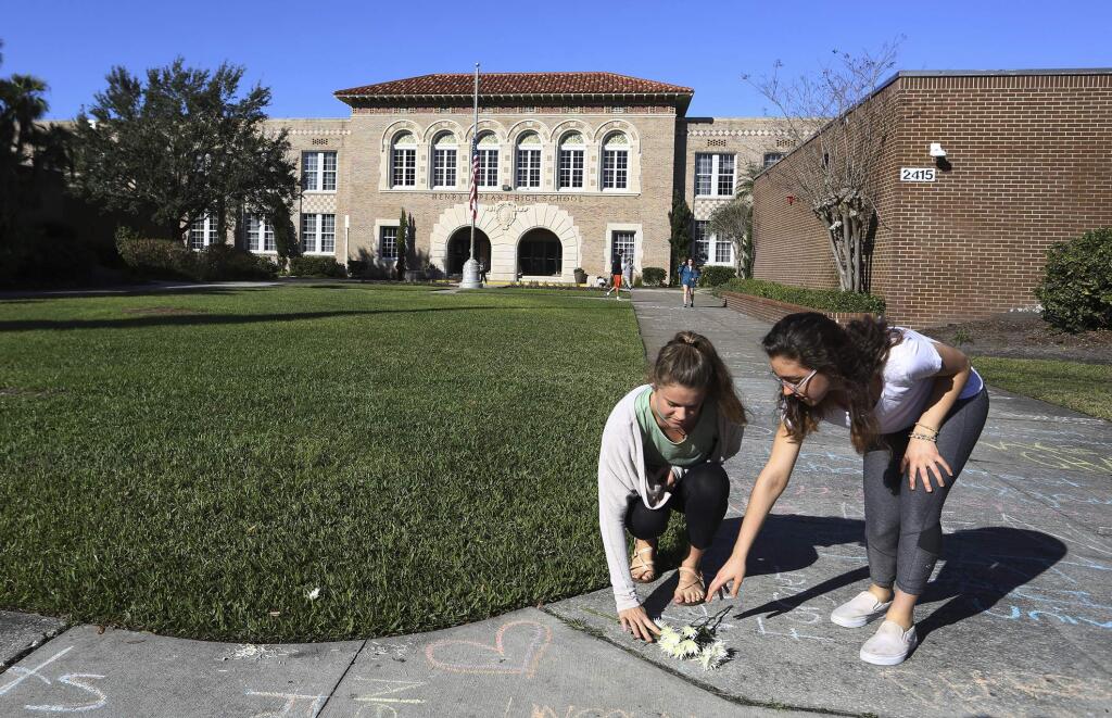Plant High School seniors Catarina Sterlacci, left, and Leigh Gabriely, right, place flowers on the sidewalk in front of their school to show support for the shooting victims Friday, Feb. 16, 2018 in Tampa, Fla. (James Borchuck/Tampa Bay Times via AP)