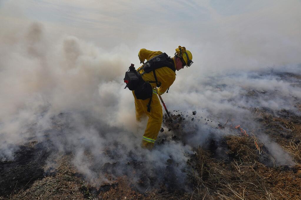 Rancho Adobe firefighter Trevor Steis pulls fuel into a burned area to protect a property along Crane Canyon Road, near Alta Monte Drive, east of Rohnert Park on Wednesday, October 11, 2017. (Christopher Chung/ The Press Democrat)
