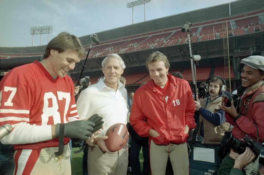 San Francisco 49ers' head coach Bill Walsh, center, shares a laugh with quarterback Joe Montana, in red jacket at right, and receiver Dwight Clark, left, during picture day at San Francisco's Candlestick Park, Jan. 16, 1985. (AP Photo)