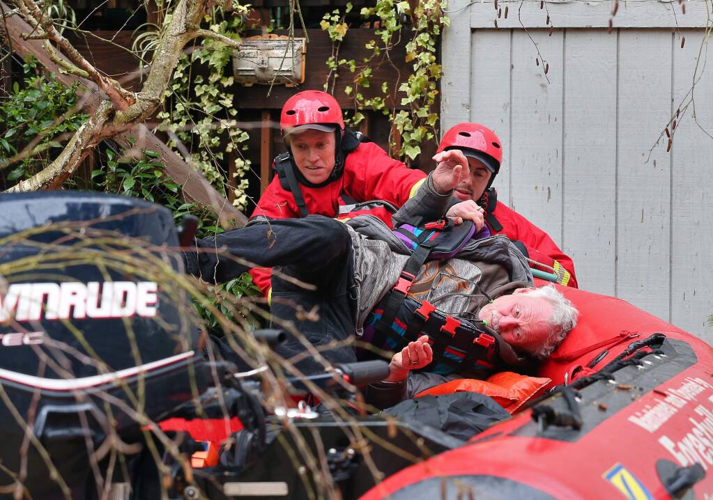 Forestville Fire Department engineers Eric Gromala, left, and Spencer Hansen load Jack Hulsey into their boat as they evacuate him from his River Drive home near Forestville on Wednesday, February 27, 2019. (Christopher Chung / The Press Democrat)