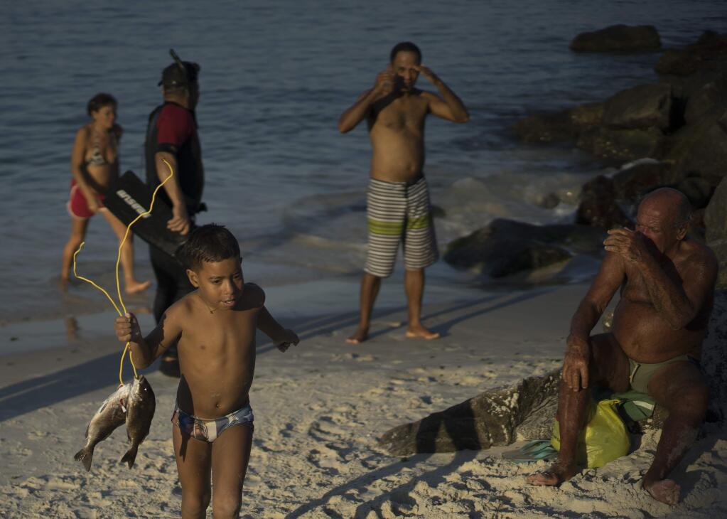 In this July 12, 2015 photo, a boy walks with his father's catch of the day from the Marina da Gloria, in Rio de Janeiro, Brazil. The head of Rio's Infectious Diseases Society said contaminated waters in beaches and lakes has led to 'endemic' public health woes among Brazilians, primarily infectious diarrhea in children. By adolescence, he said, people in Rio have been so exposed to the viruses in the water their bodies build up antibodies. But foreign athletes and tourists wont have that protection. (AP Photo/Leo Correa)