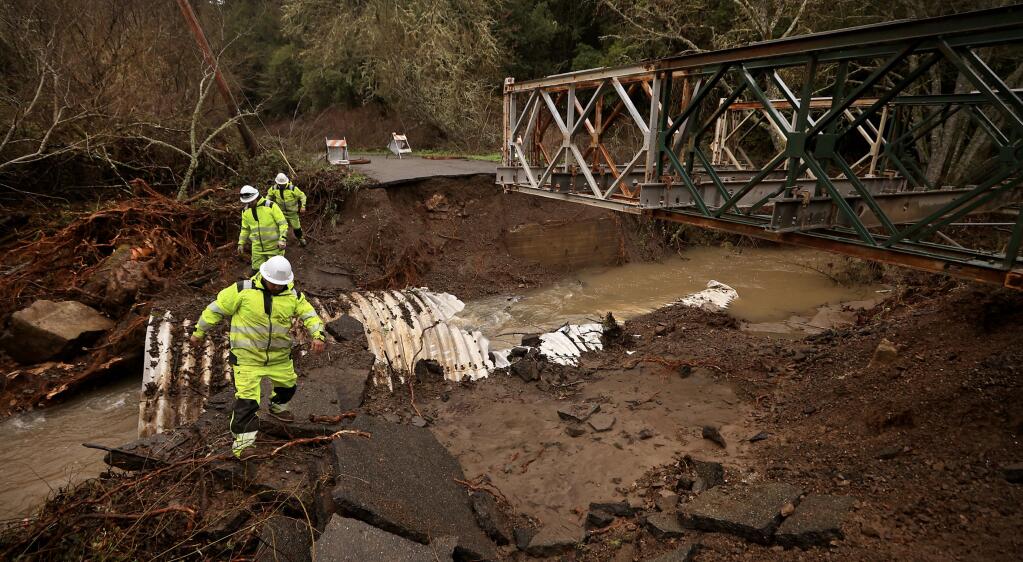 A Sonoma Public Infrastructure crew scrambles across the washed out portion of Salmon Creek Road near Bodega, Tuesday, Jan. 10, 2023, after a flash flood on Salmon Creek. A Bailey bridge, right, is being constructed to span the creek for residents that have been cut off. (Kent Porter/The Press Democrat)